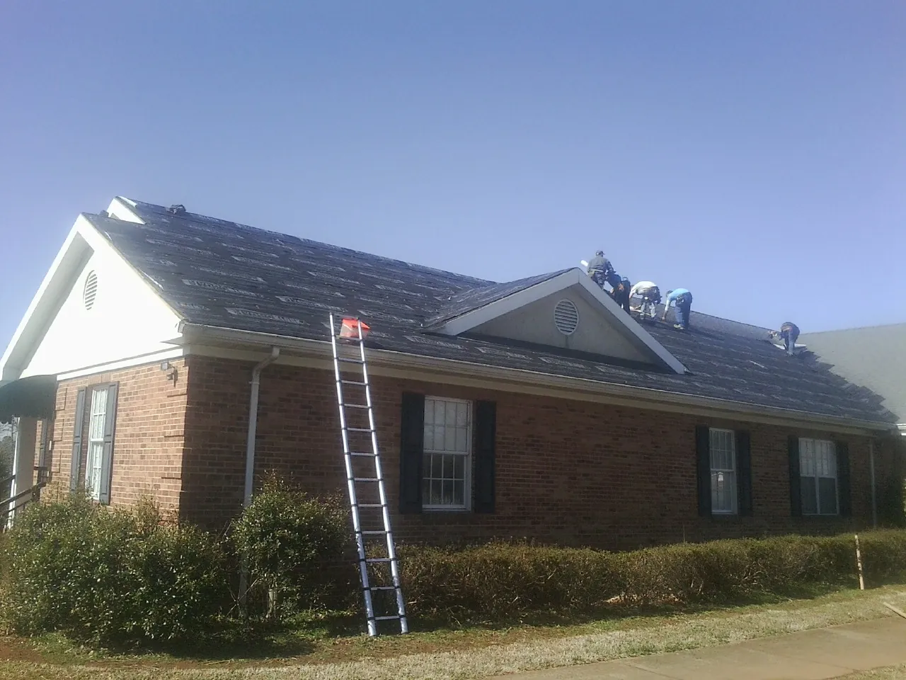 Crew tearing shingles off a brick ranch roof with a ladder set — Metal Roof Repair work by our crew in Freeland