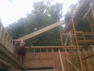 Carpenter raising a rafter beam on a new second story frame in Freeland