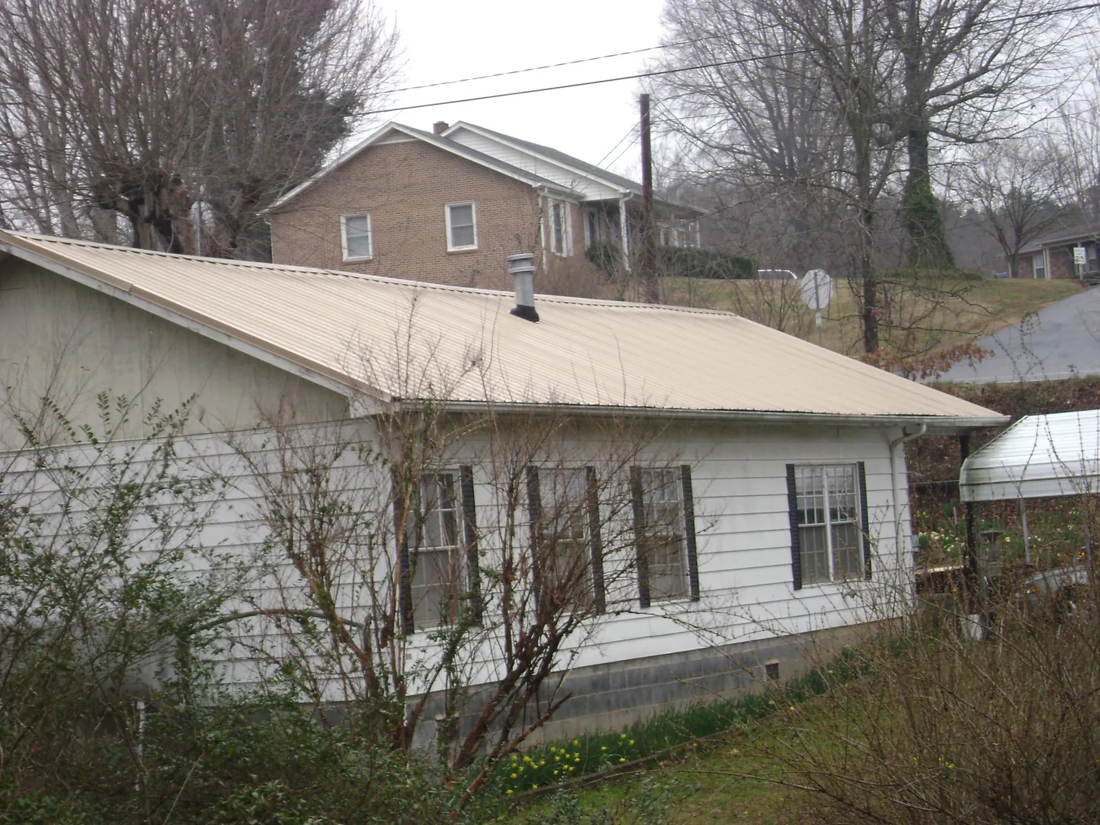 Tan metal roof on a white sided house set into a hillside — Commercial Roofing by Roofing Brothers in Freeland