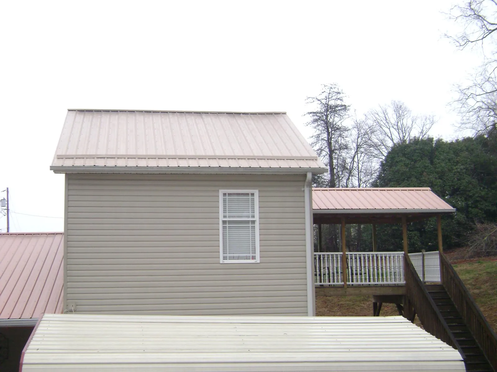 Tan metal roofs on a two story addition and attached porch, from a Roof Replacement job in Freeland